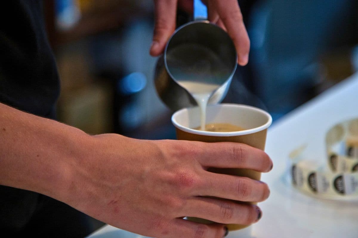 A close up if a barista's hands pouring milk into coffee