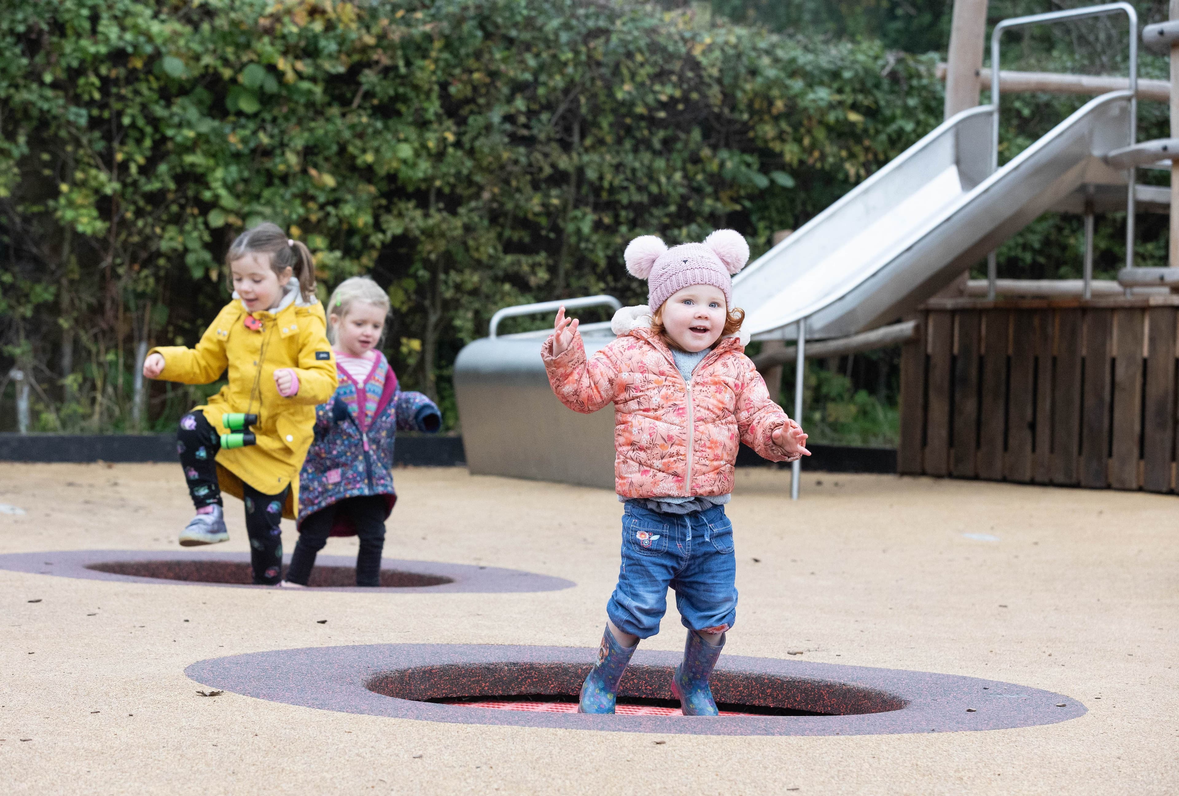 Little girl aged two, dressed in winter clothing, jumping on a ground trampoline